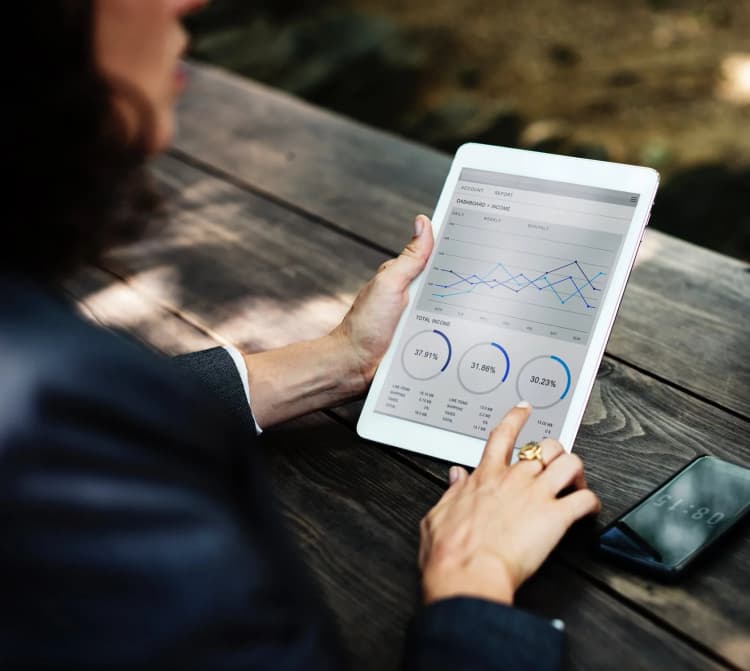 woman at a table outside holding a tablet showing charts