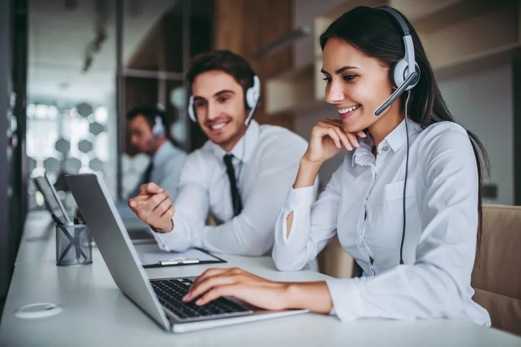 woman typing on a computer, smiling and talking to a customer on a headset