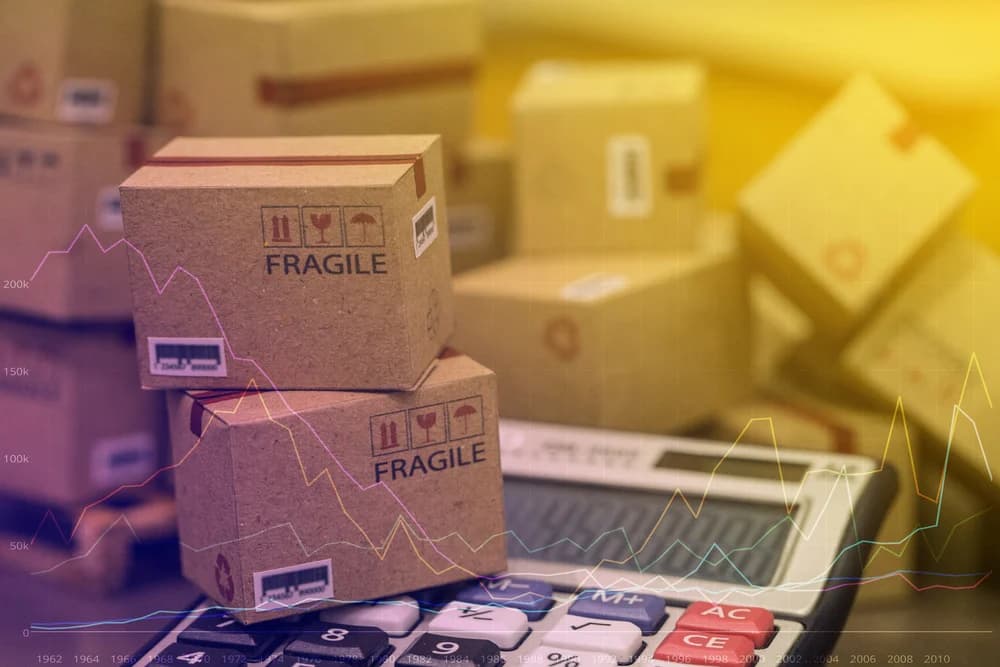 Fragile shipping boxes stacked on calculator with business growth charts overlay
