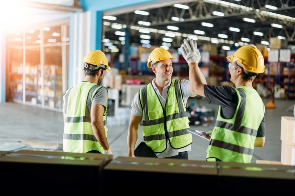 Warehouse workers in safety vests and hard hats celebrating successful WMS implementation