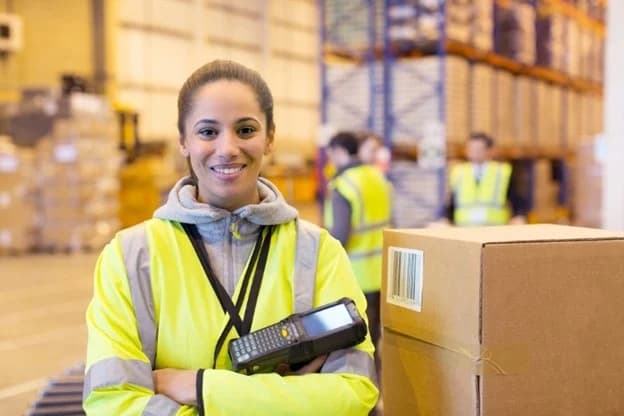 Smiling warehouse worker in safety vest holding barcode scanner in fulfillment center