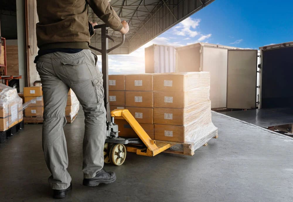 Warehouse worker using pallet jack to move packaged boxes for pick and pack operations