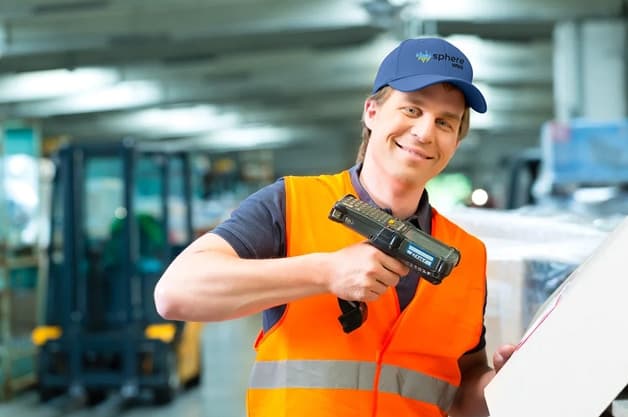 Smiling warehouse worker in blue hat and safety vest holding handheld scanner