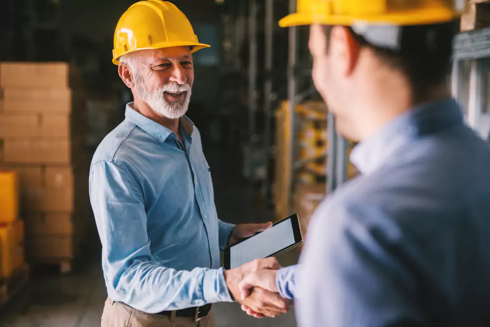 two men in hard hats shaking hands in a warehouse