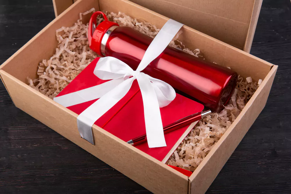 a box with a thermos, notepad, and pen with a bow around it