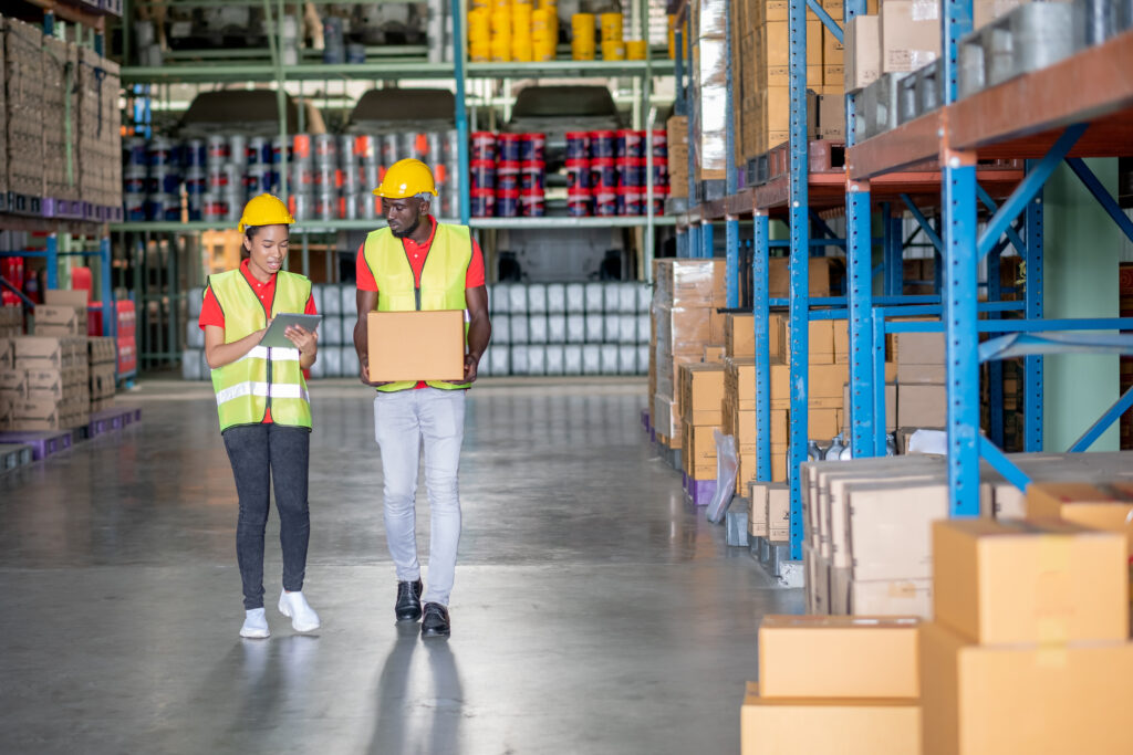 warehouse workers talking and walking in an aisle one holding a tablet another person holding a box