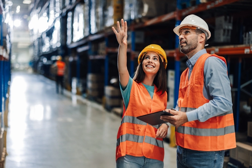 two warehouse workers pointing to a warehouse shelf one of them holding a tablet