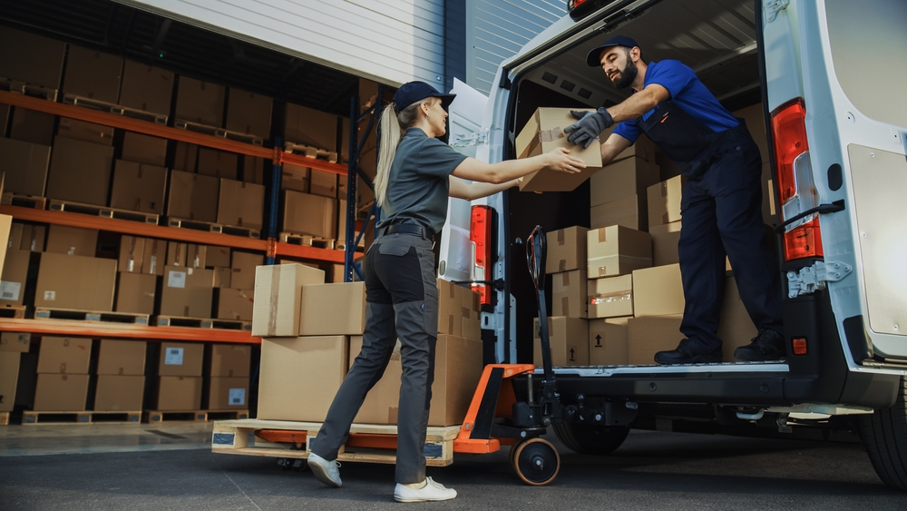 woman handling boxes to a carrier to deliver to customers with a background of warehouse shelving with boxes