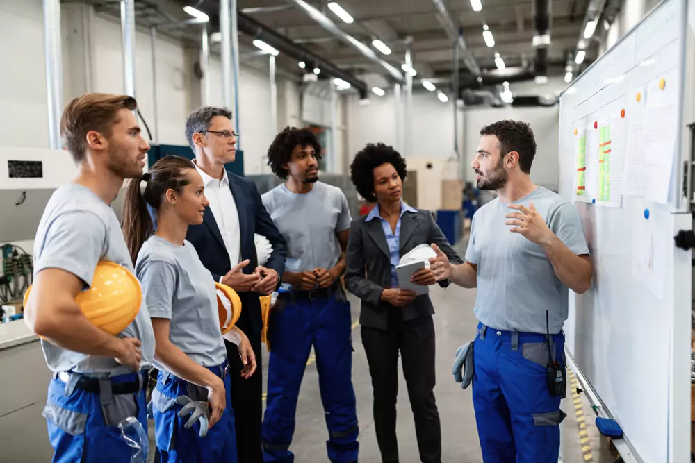 manager talking to warehouse employees with a dry erase board in the background